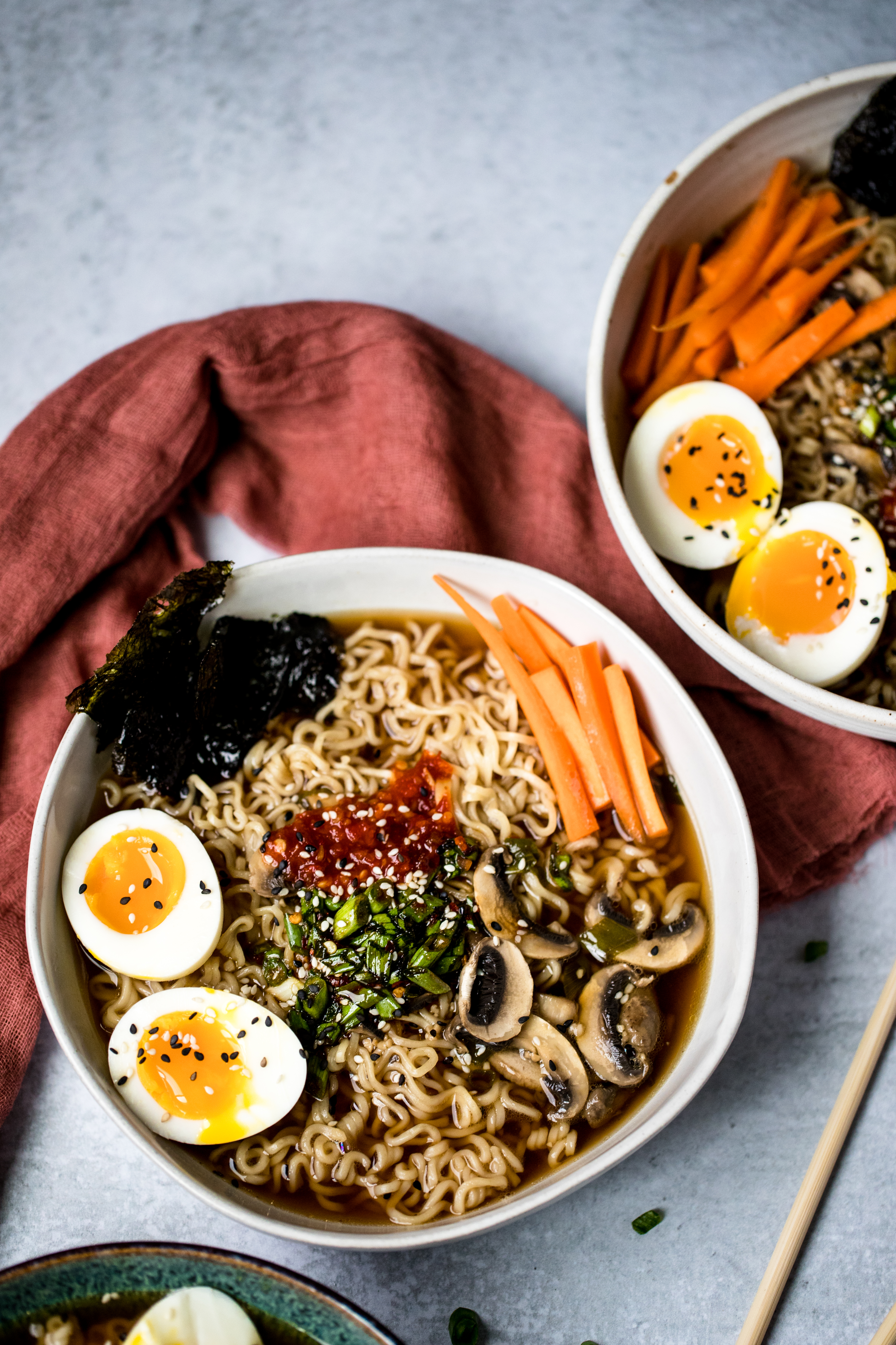 two bowls of vegetarian ramen topped with soft-boiled eggs, sliced carrots, seaweed, and green onions