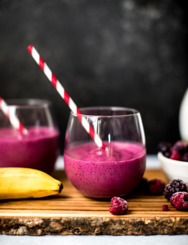 a blueberry beet smoothie in a wine glass with a red straw