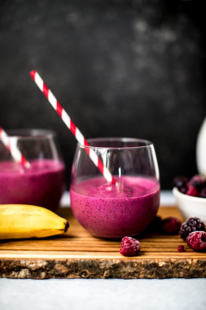 a blueberry beet smoothie in a wine glass with a red straw