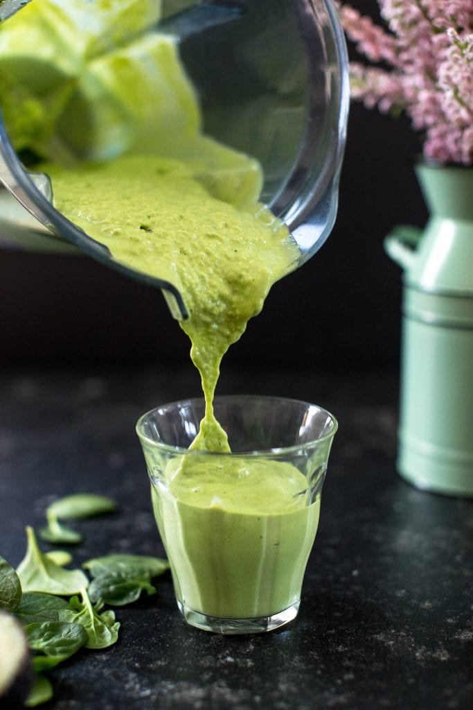 a green smoothie being poured from a vitamix into a glass cup 