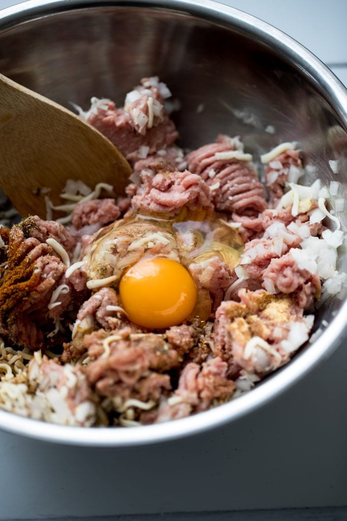 ground turkey in a stainless steel bowl with an egg getting mixed in