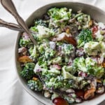 Broccoli salad in a white bowl on a white linen