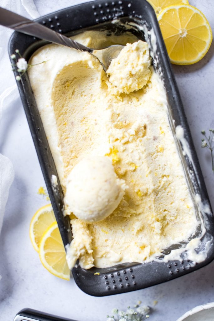 lemon ice cream in a container being scooped with an ice cream scooper