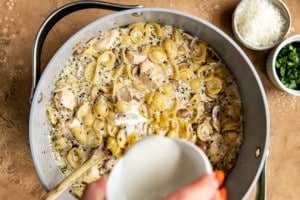 pouring milk into pasta and chicken mixture in dutch oven pan