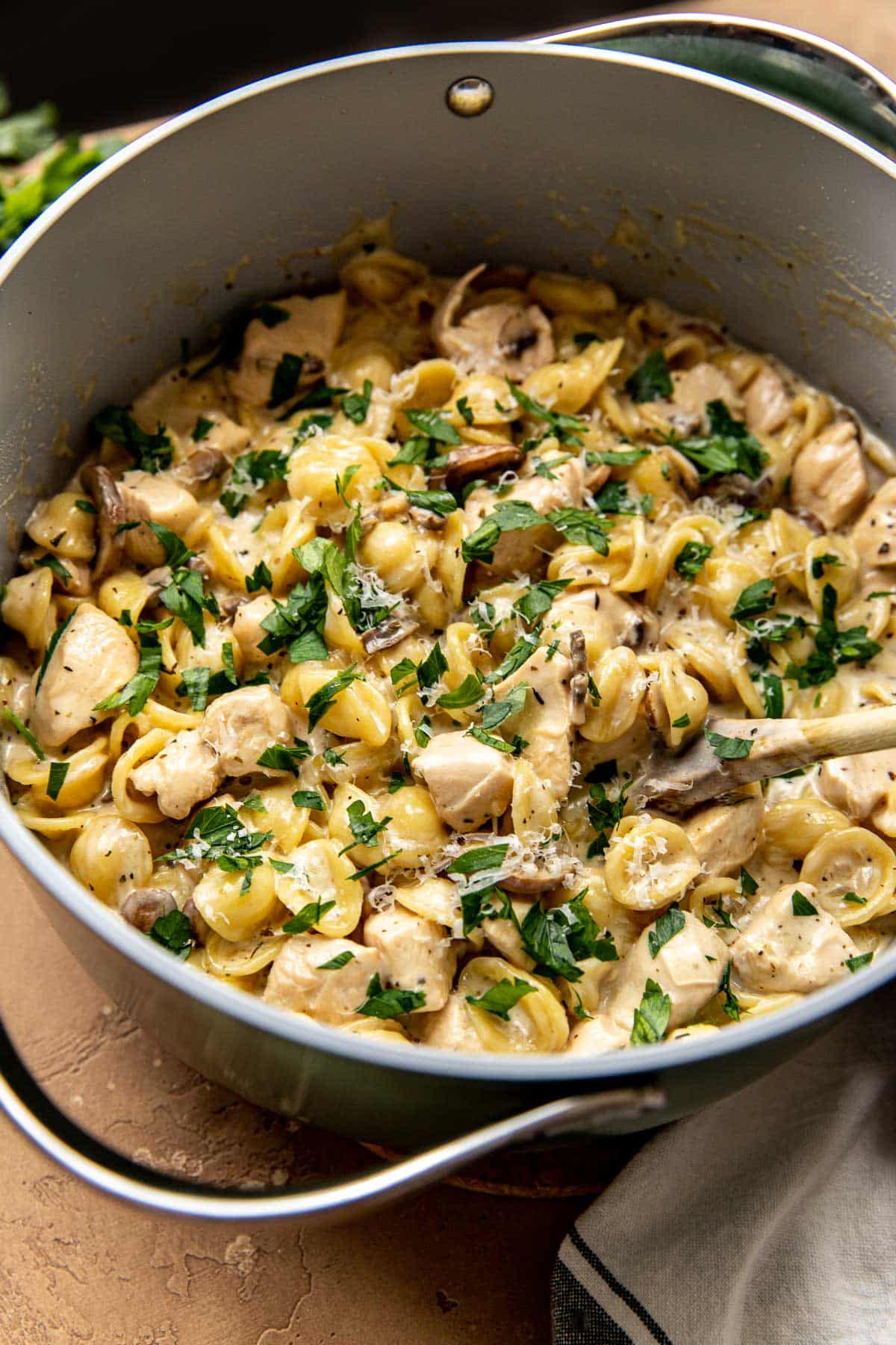 pasta with chicken, mushrooms, and green herbs in a dutch oven pan
