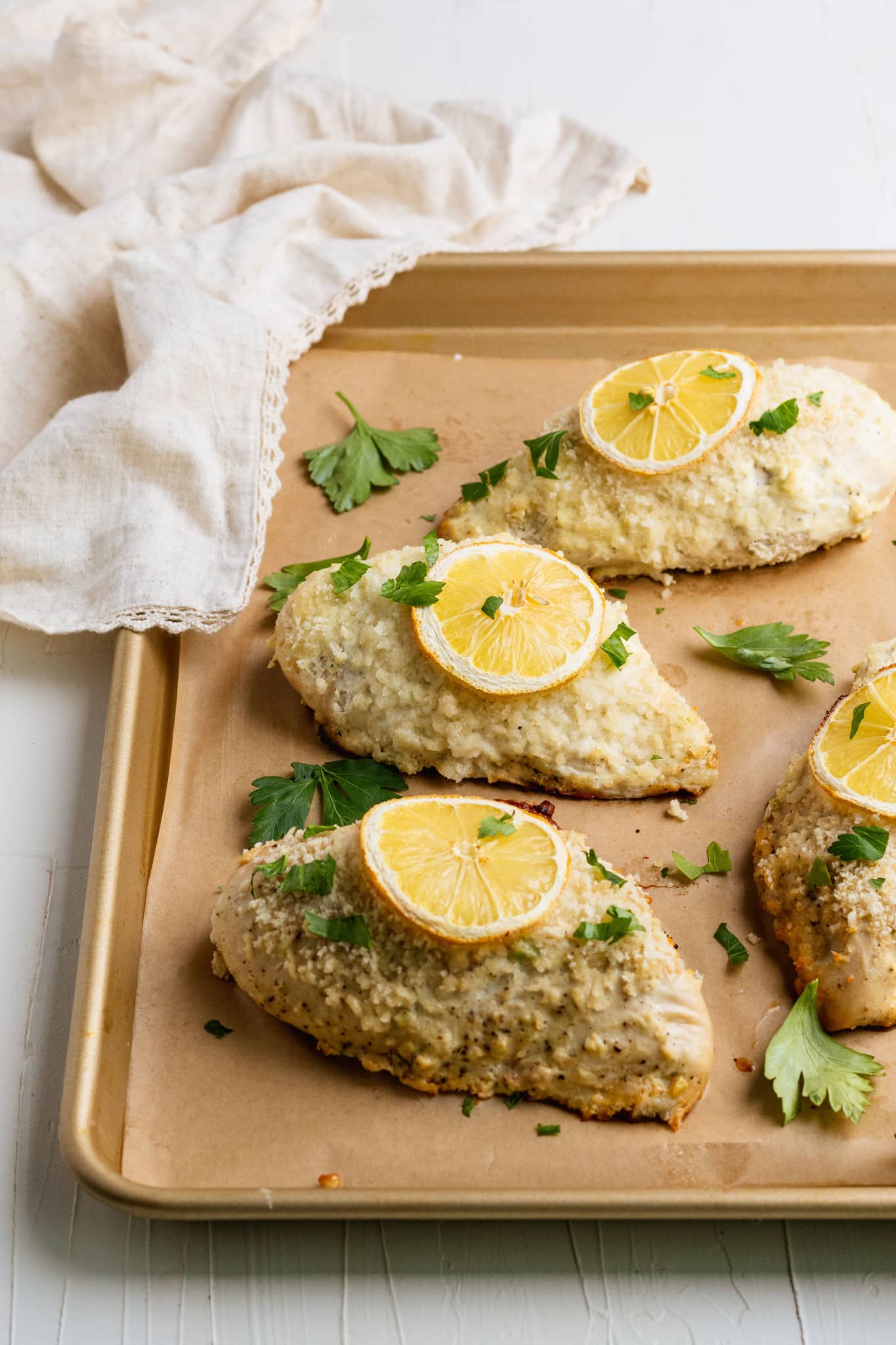 baked chicken on a sheet pan lined with parchment paper and a lemon slice