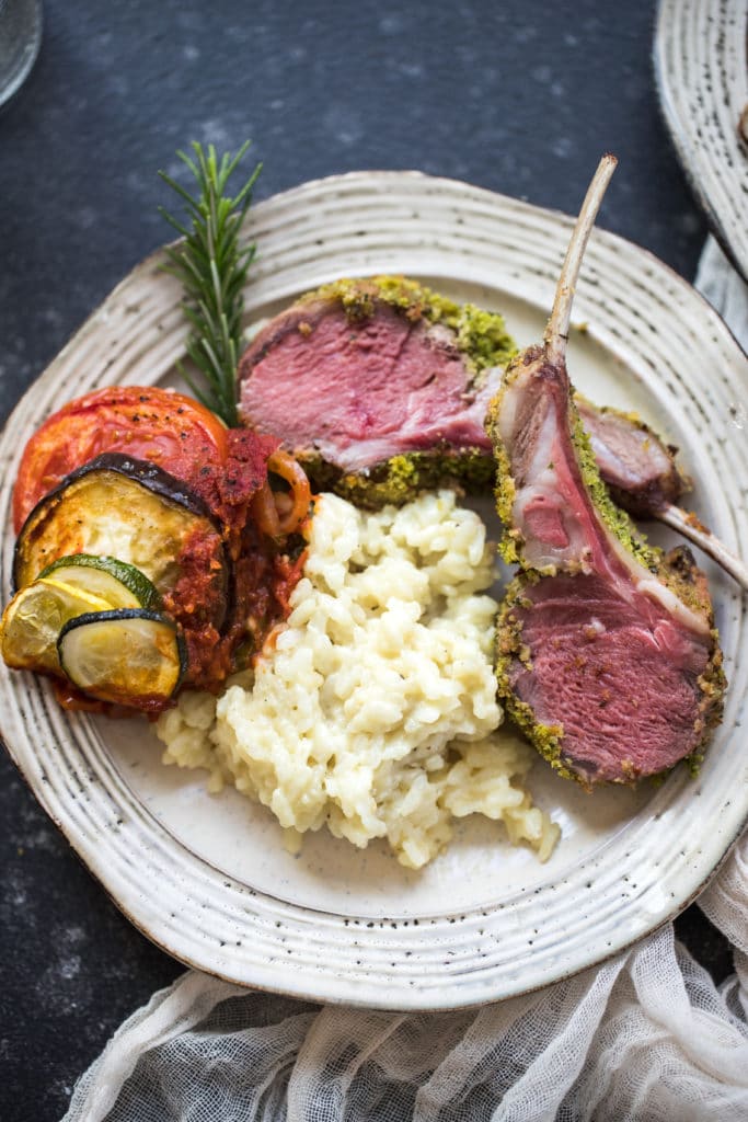 herb crusted rack of lamb with risotto and veggies on a white plate