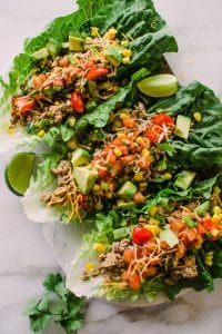 three romaine lettuce leaves filled with a ground turkey mixture with avocado, shredded cheese, corn, and salsa