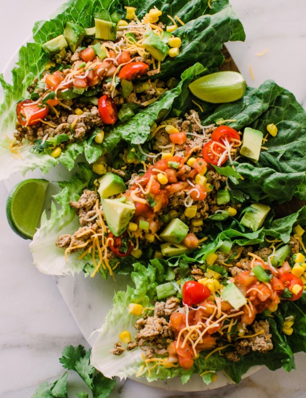 three romaine lettuce leaves filled with a ground turkey mixture with avocado, shredded cheese, corn, and salsa