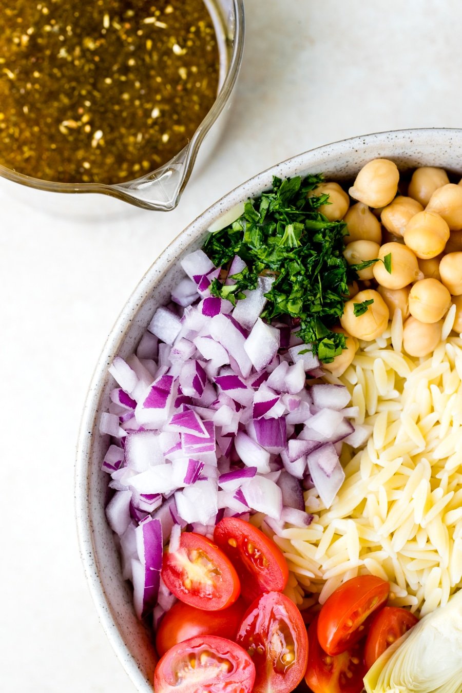 Orzo Salad Recipe in a large white bowl with red onion, cherry tomatoes, parsley and garbanzo beans