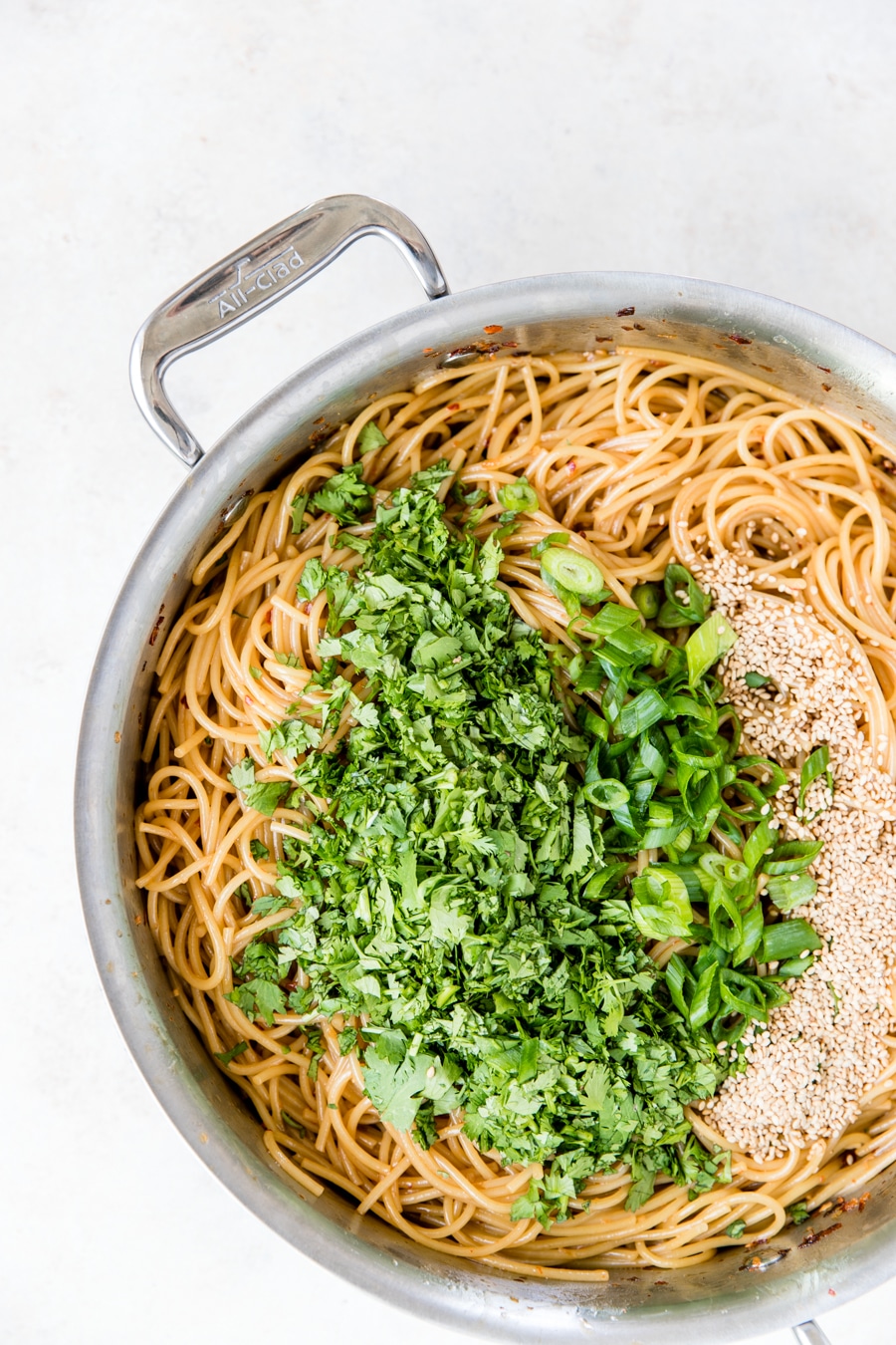 a pan filled with kung pao noodles topped with cilantro, green onions and sesame seeds