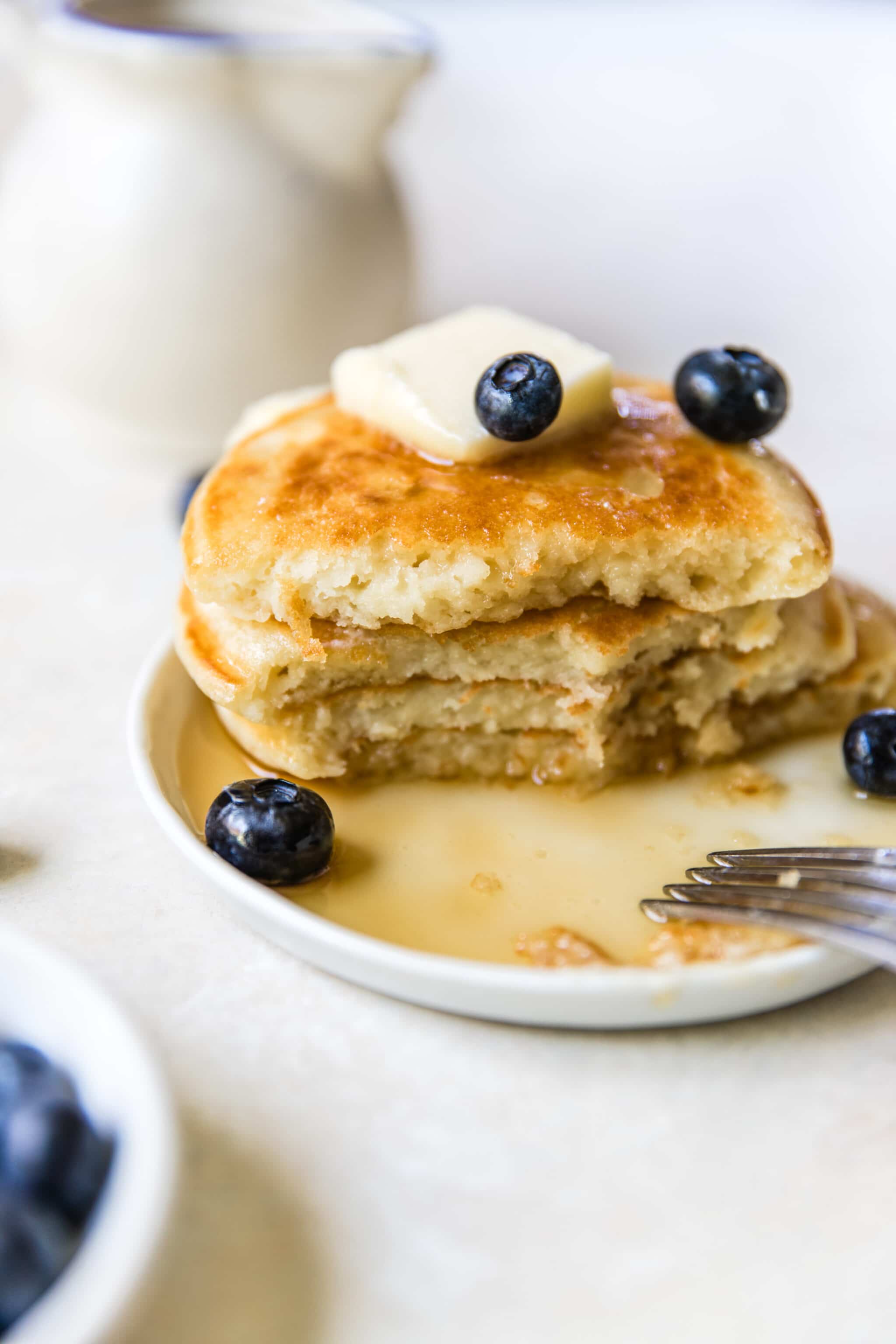buttermilk pancakes on a white plate topped with butter and blueberries