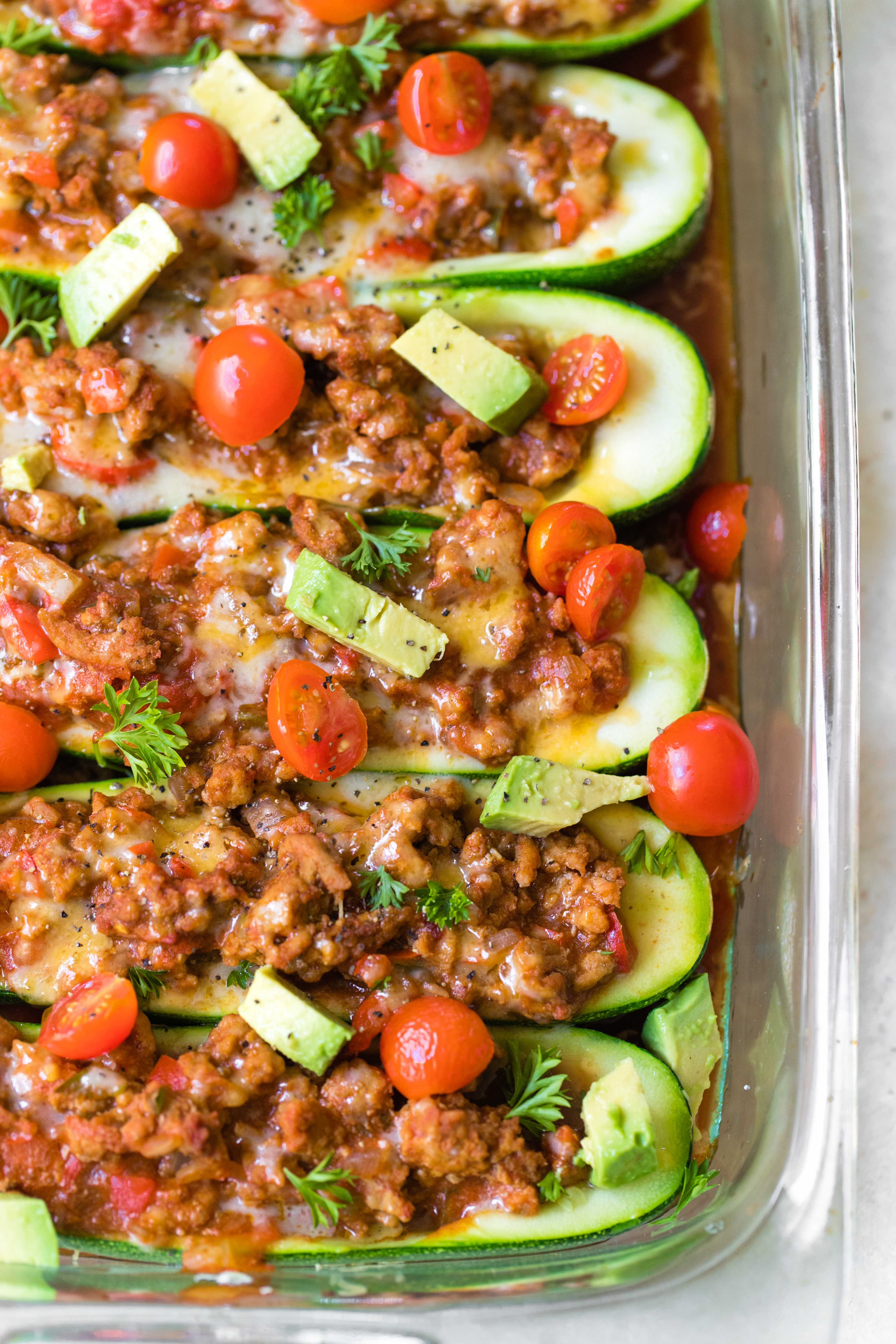 zucchini taco boats in a glass Pyrex dish topped with avocado and tomatoes 