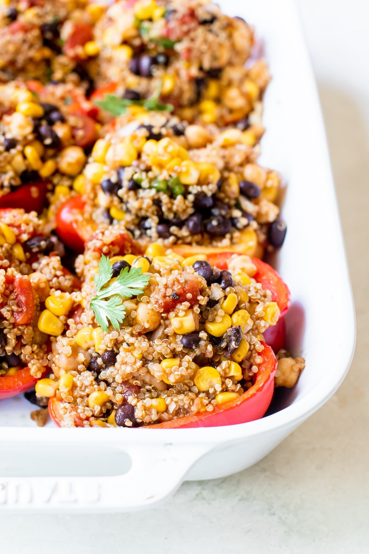 A white dish with bell peppers stuffed with a mixture of quinoa, black beans, corn, and tomatoes