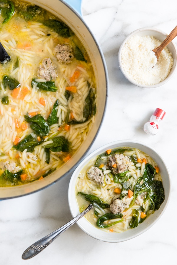 Italian wedding soup in a white bowl with Parmesan cheese on the side