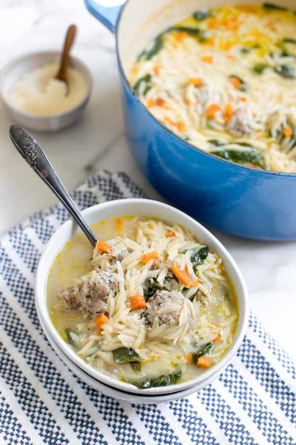 Italian wedding soup in a white bowl with Parmesan cheese on the side