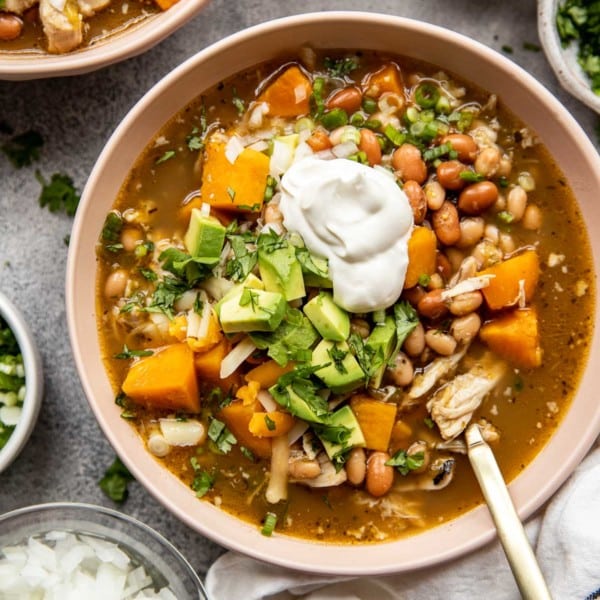tan bowl of chicken chili soup topped with avocado and sour cream