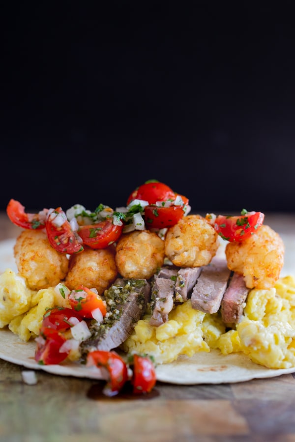 a breakfast burrito with carne asada steak, eggs, pico de gallo, tater tots and cheese