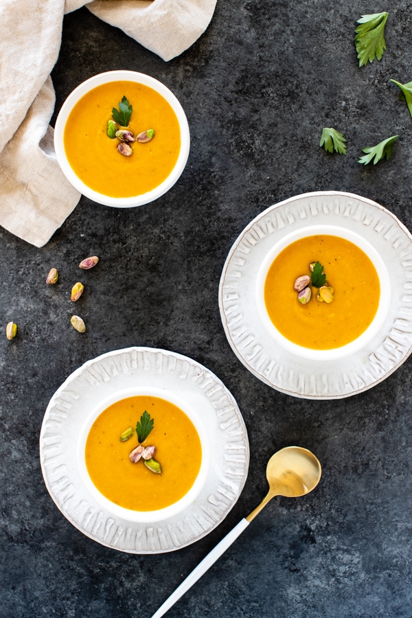 pistachio pumpkin soup in small white bowls topped with pistachios 