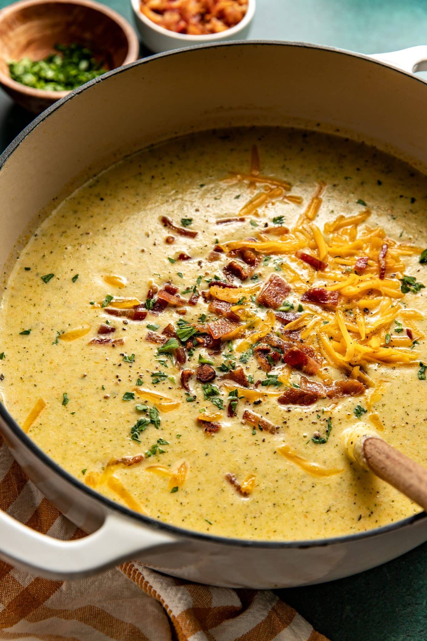 a large dutch oven pot filled with broccoli cauliflower soup topped with bacon, parsley, and cheddar cheese. 