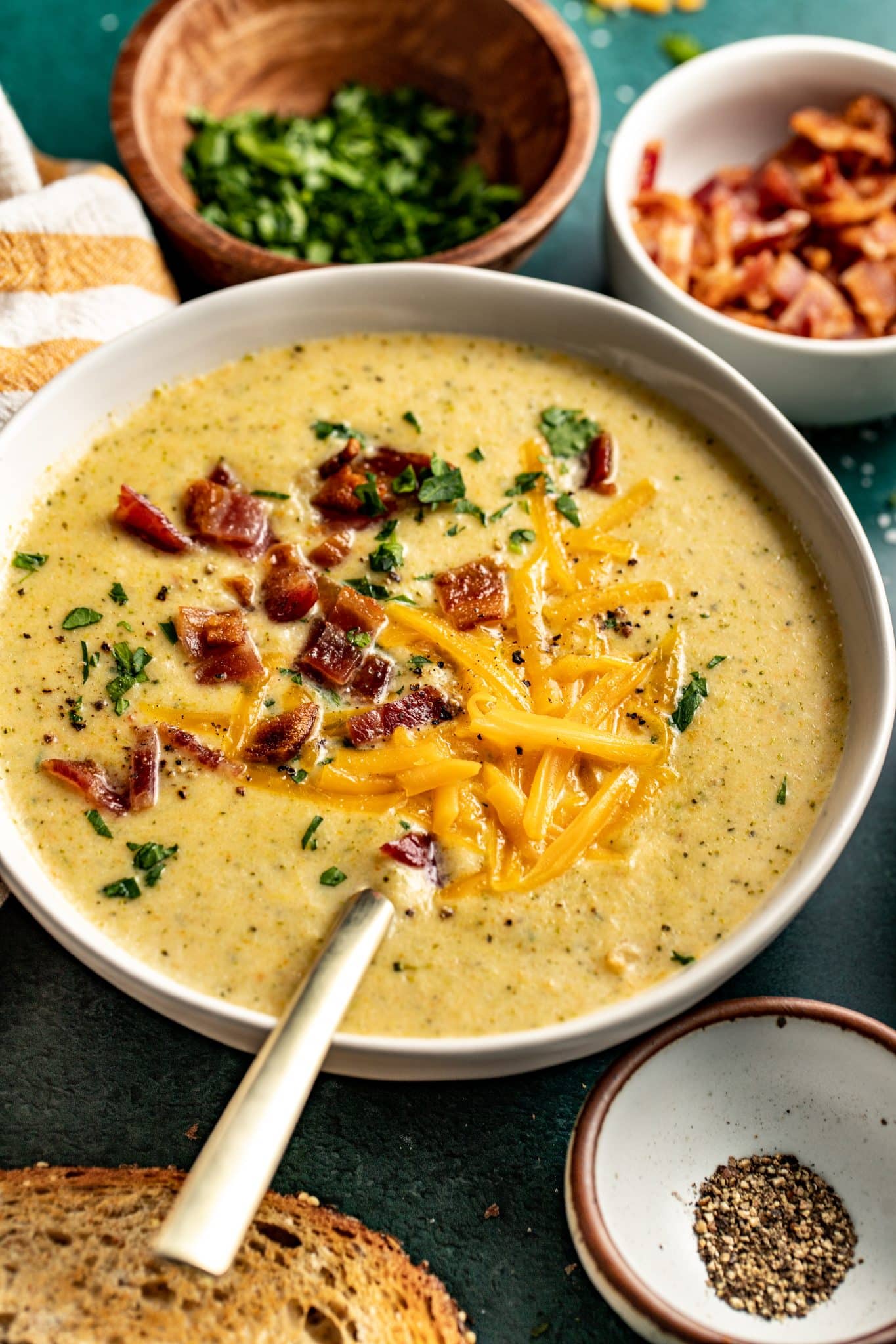 a bowl of broccoli soup in a white bowl topped with bacon and cheddar cheese. 