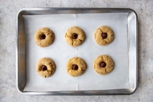 six almond butter blossom cookies on a baking tray with candy kisses inserted on top