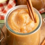 Close-up of a jar of applesauce topped with a cinnamon stick, sprinkled with ground cinnamon.