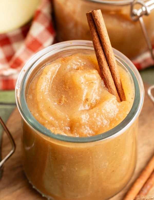 Close-up of a jar of applesauce topped with a cinnamon stick, sprinkled with ground cinnamon.