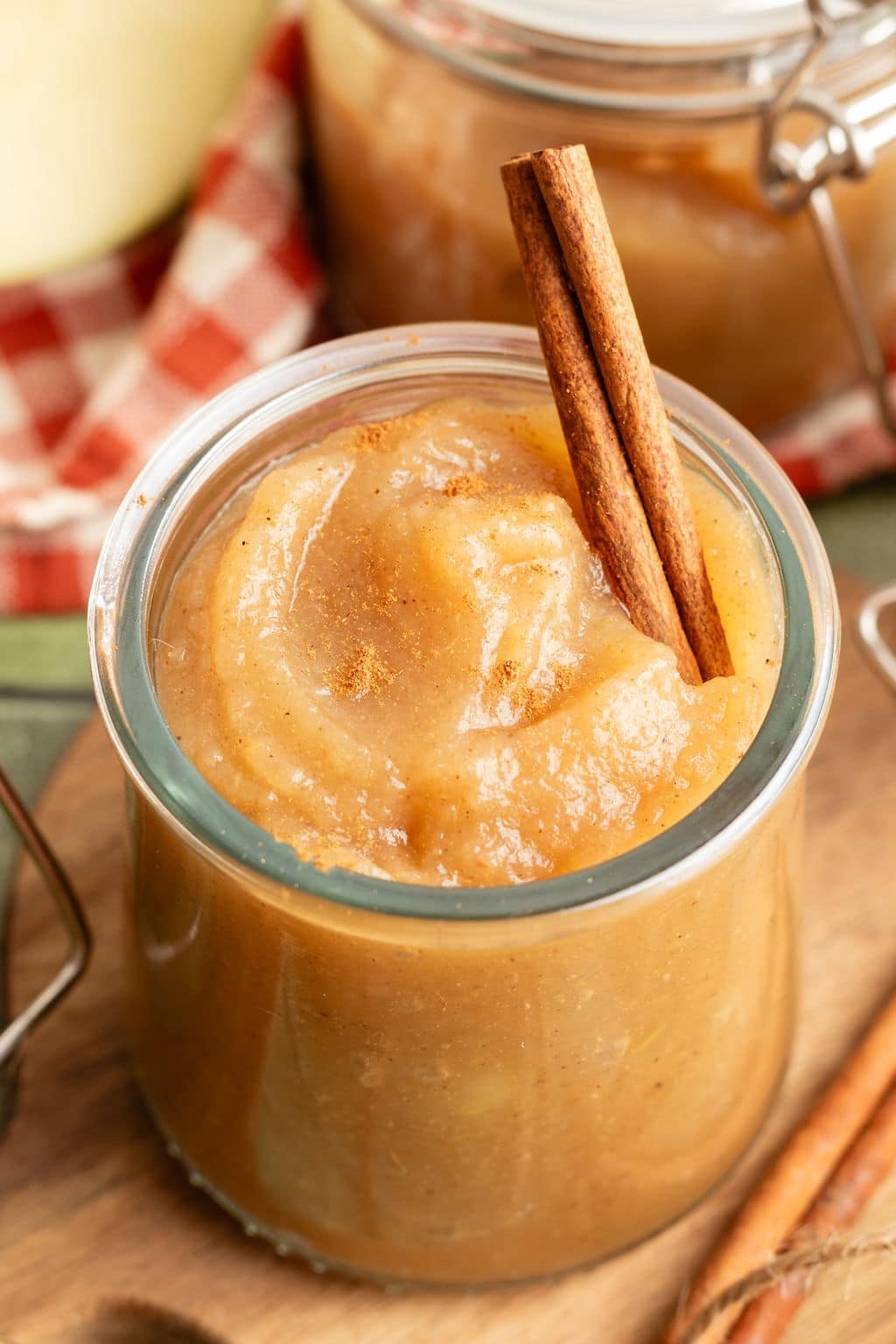 Close-up of a jar of applesauce topped with a cinnamon stick, sprinkled with ground cinnamon.