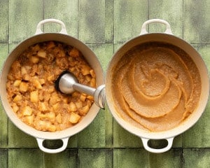 Apples cooking down in a large pot, partially mashed, with an immersion blender blending the mixture into smooth applesauce.