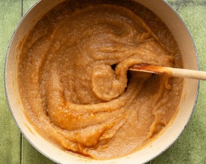 Freshly blended homemade applesauce in a large pot, thick and smooth, with a wooden spoon stirring the mixture.