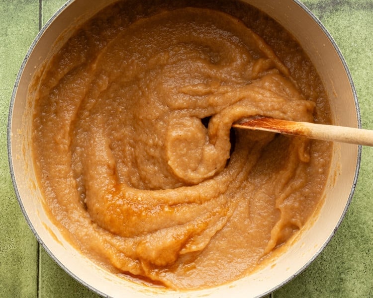 Freshly blended homemade applesauce in a large pot, thick and smooth, with a wooden spoon stirring the mixture.