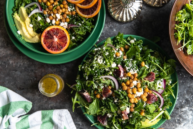 a winter blood orange salad with massaged kale and arugula on a green plate topped with mint and chickpeas