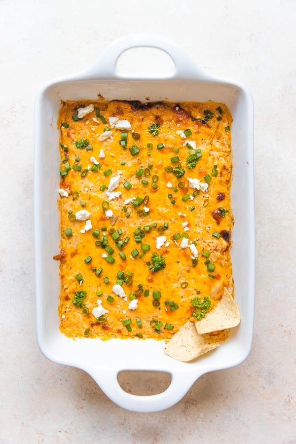 buffalo chicken dip in a white baking dish topped with feta cheese and green onions