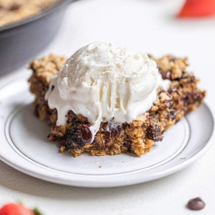 a slice of an oatmeal raisin chocolate chip cookie skillet on a white plate with vanilla bean ice cream