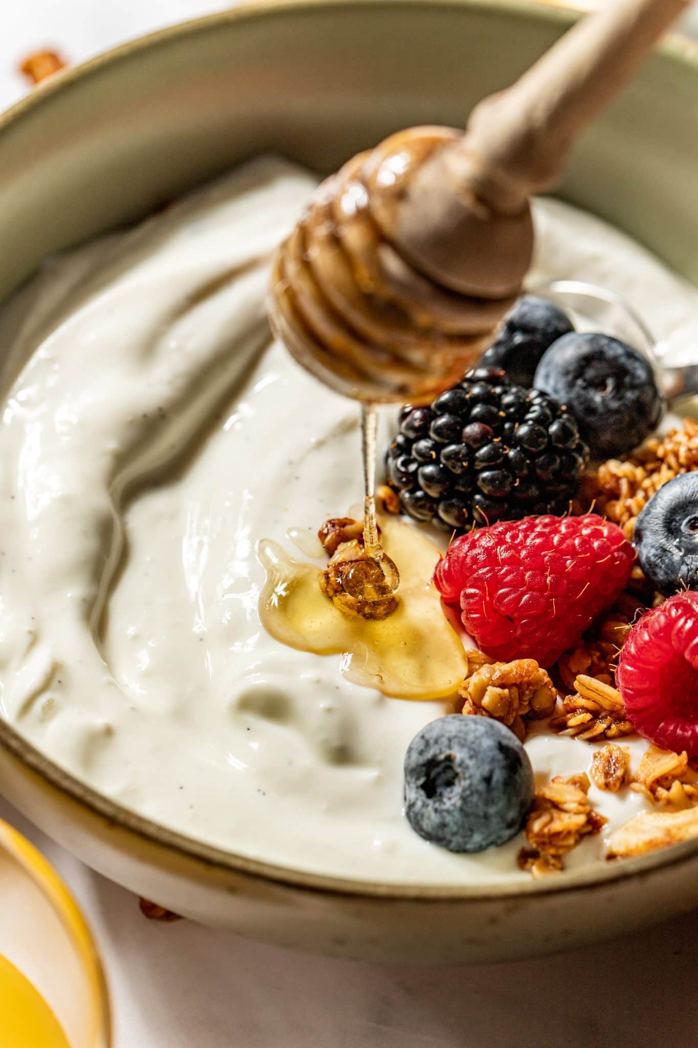 honey being drizzled on top of a bowl of yogurt with fresh berries on top. 