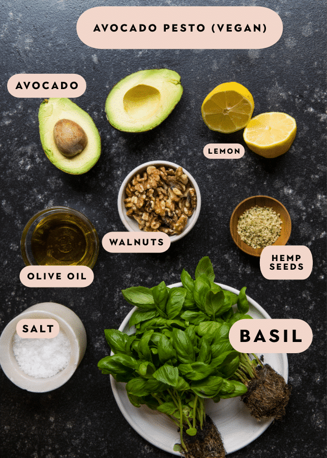 ingredients in small bowls to make an avocado pesto on a black board