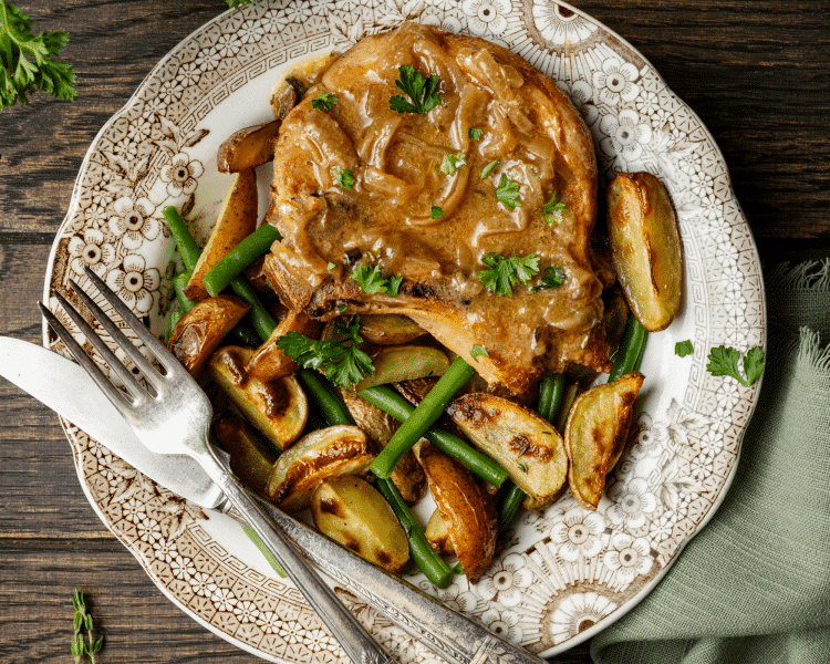 Slow cooker pork chop on plate with potatoes and green beans.