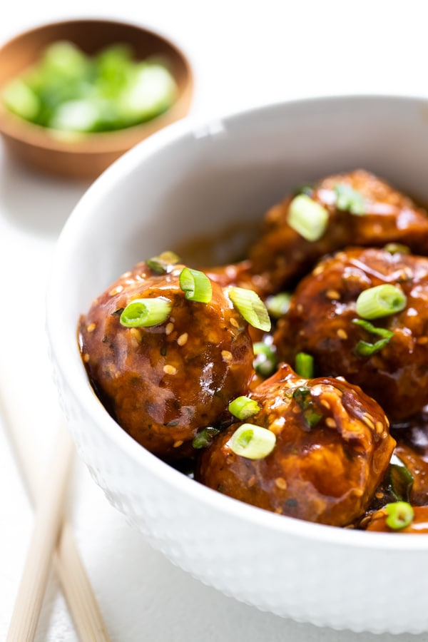 healthy meatballs in a white bowl topped with green onions and sesame seeds