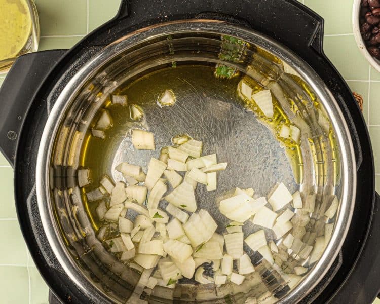 Overhead shot of the inside of an Instant pot with pieces of cut up onion and olive oil.