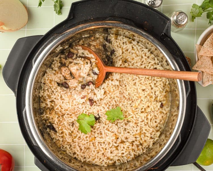 Overhead view of the inside of an instant pot with cooked rice, chicken, black beans, and spices, and wooden spoon pulling out a small serving.