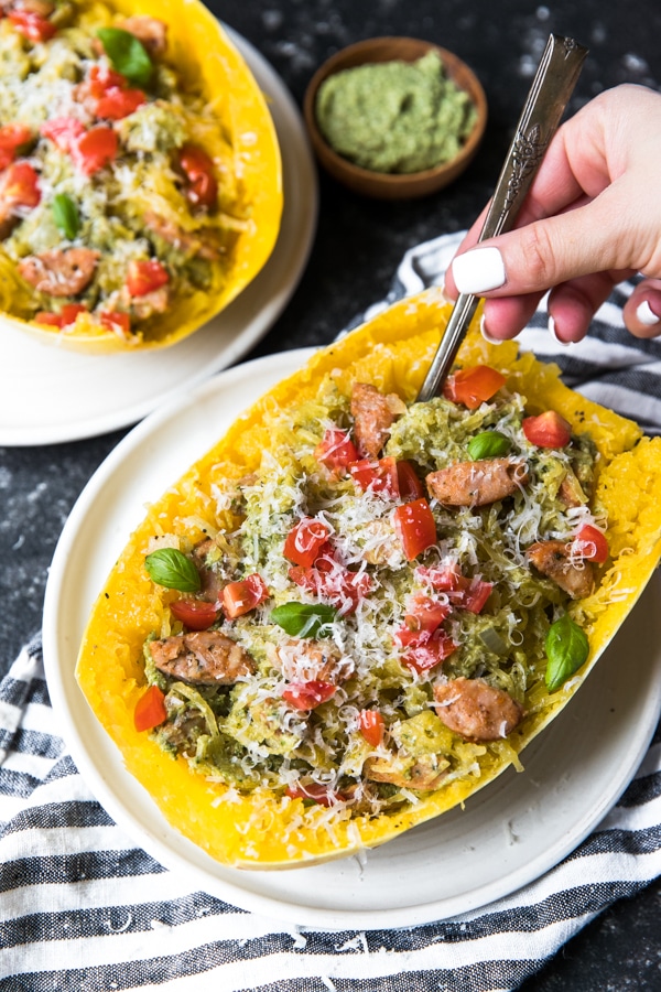 spaghetti squash boats filled with chicken sausage, vegan avocado pesto and topped with cherry tomatoes and basil in a white bowl