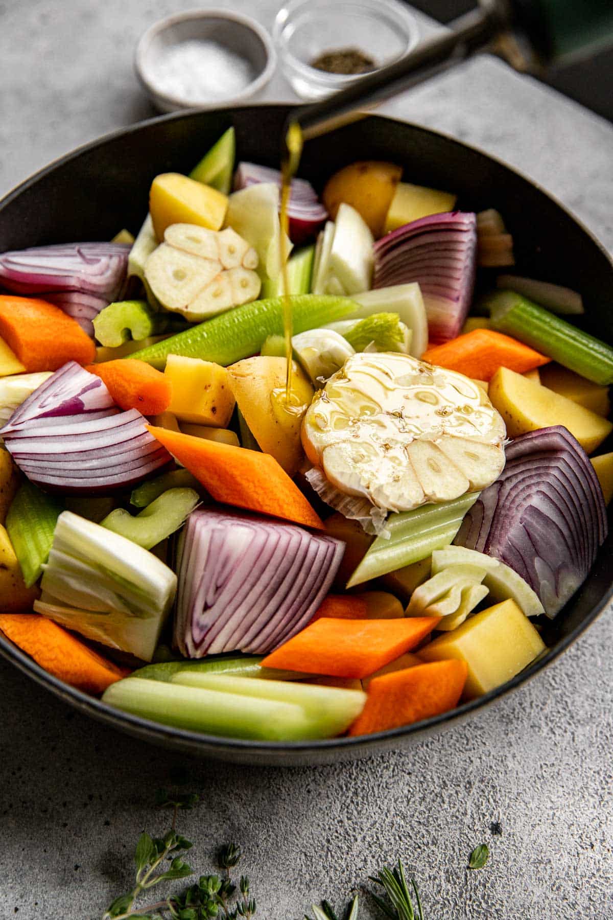 a variety of veggies in a roasted pan being coated in olive oil. 