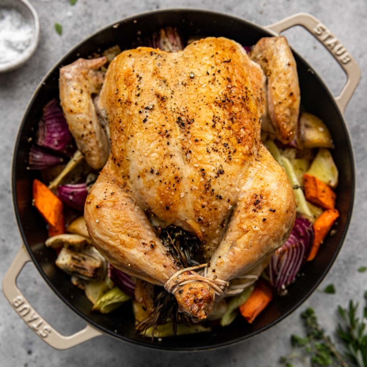 full roasted chicken in a dutch oven surrounded by roasted vegetables