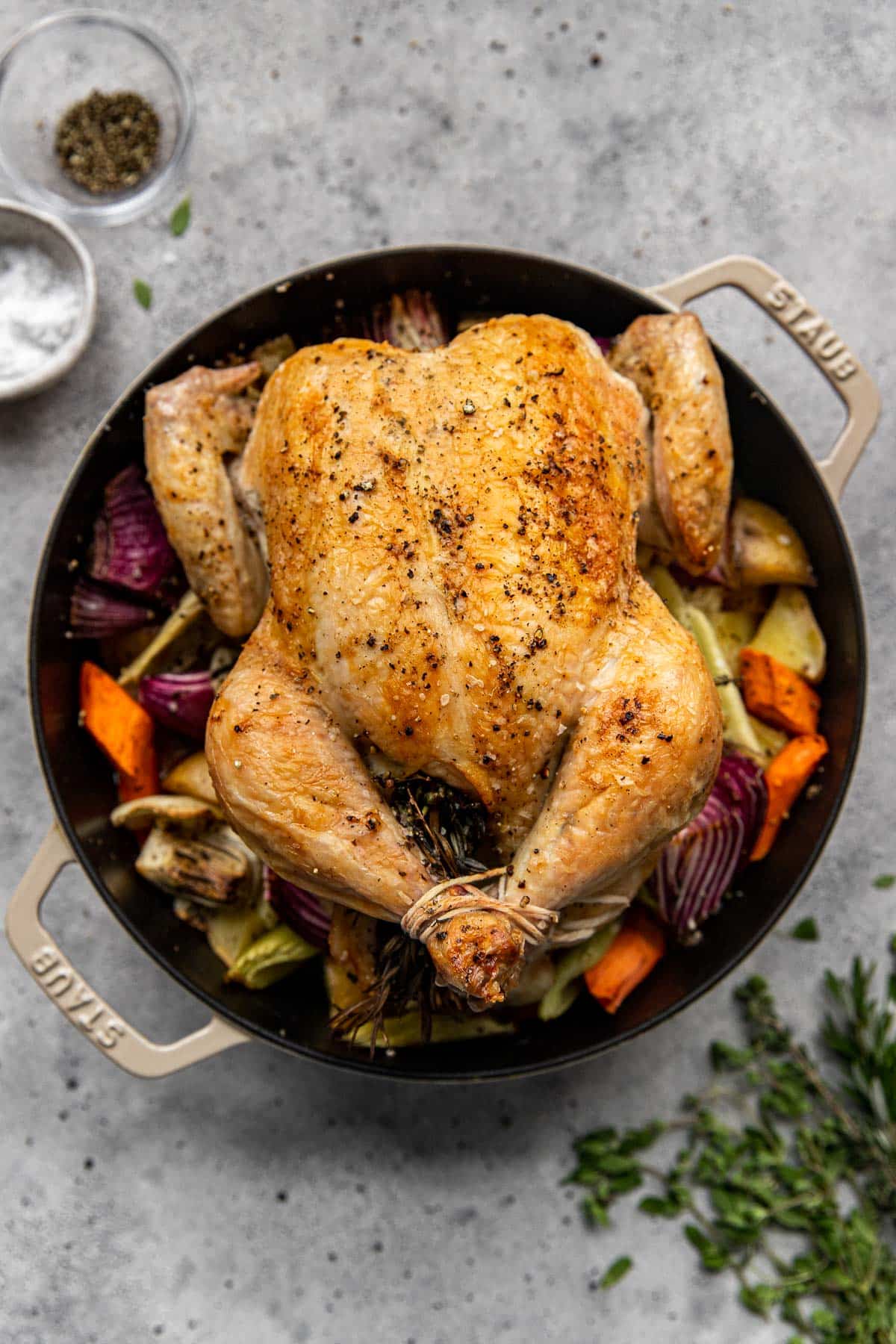 full roasted chicken in a dutch oven surrounded by roasted vegetables