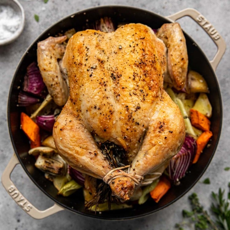 whole chicken roasted with roasted vegetables in a black cast iron dutch oven