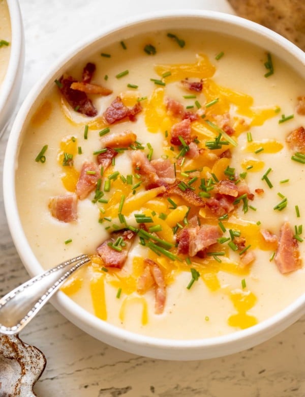 baked potato soup in a white bowl garnished with bacon, cheese and chives.
