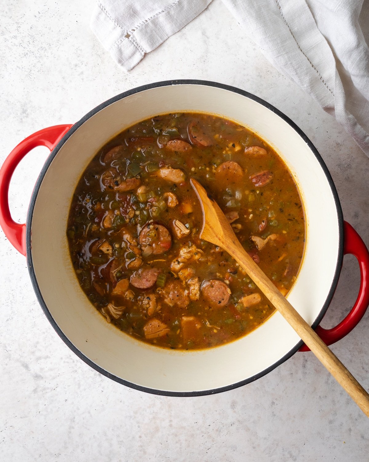 Gumbo in a Dutch oven with a wooden spoon stirring it. 