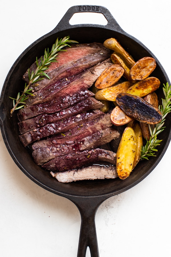 baked flank steak and fingerling potatoes in a cast iron skillet