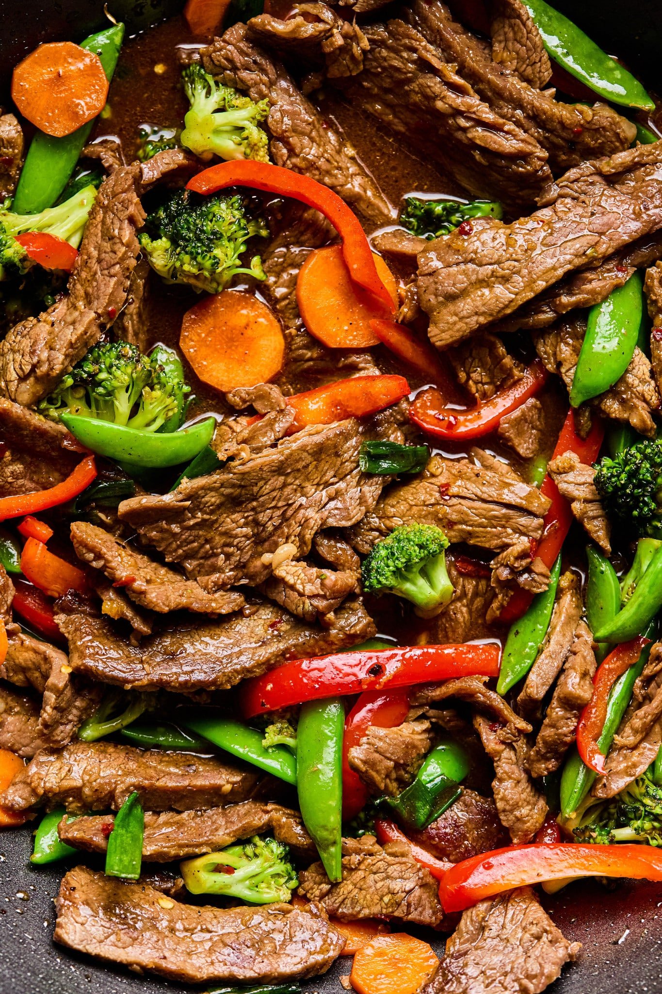 Tight close-up shot of the stir fry inside the wok, highlighting juicy beef strips, crisp vegetables, and a rich brown sauce.